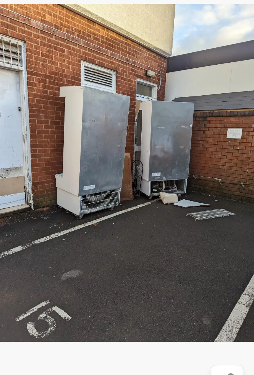 Two large upright fridges standing outside against a brick wall